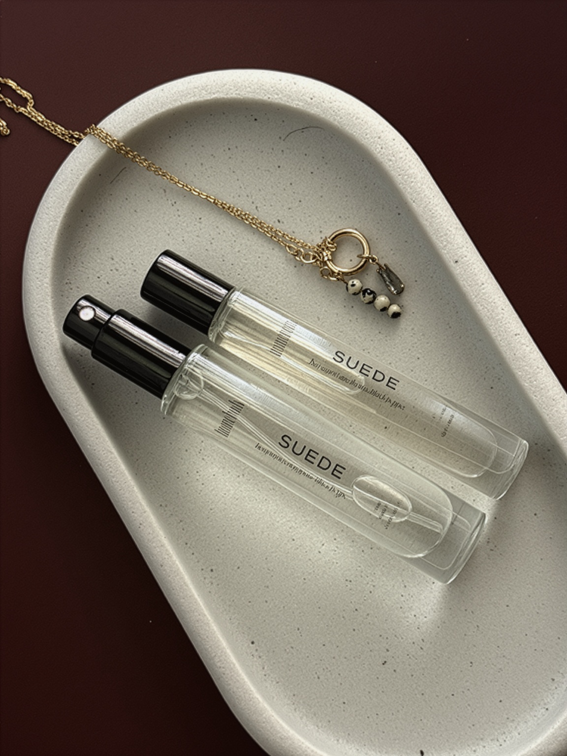 Suede perfume bottle on a white dish with jewelry
