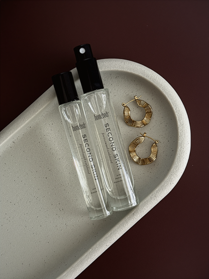 Two clear Second Skin bottles with black caps on a beige dish with gold hoop earrings.